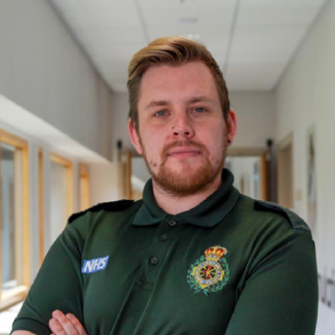 A student wearing a paramedic uniform looks into the camera with their arms folded in front of them.