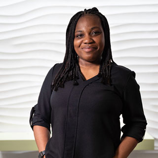 A person smiling at the camera, standing in front of a white background with a wave pattern on it.