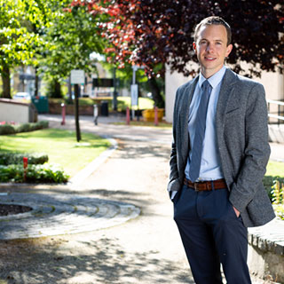 A person wearing a suit, standing in the Peace Garden on the University of Bradford campus.