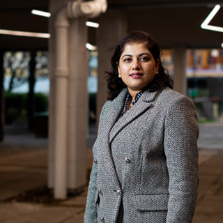 A smartly dressed student standing outside in a well-lit sheltered area.