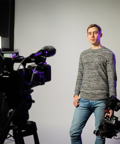 A student holding a camera being filmed by a camera