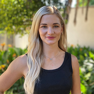 A student smiling in front of a garden illuminated by sunlight