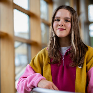 Student with arm resting on railing and smiling at camera