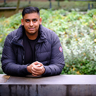 Zubayr sat at a stone bench in front of some greenery.